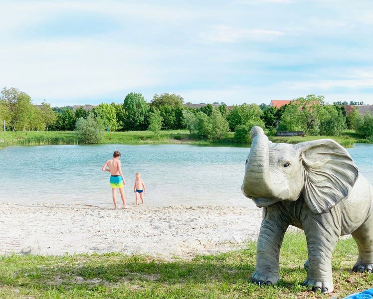 Letná fotografia dvoch deti v jazere, socha slona v rohu