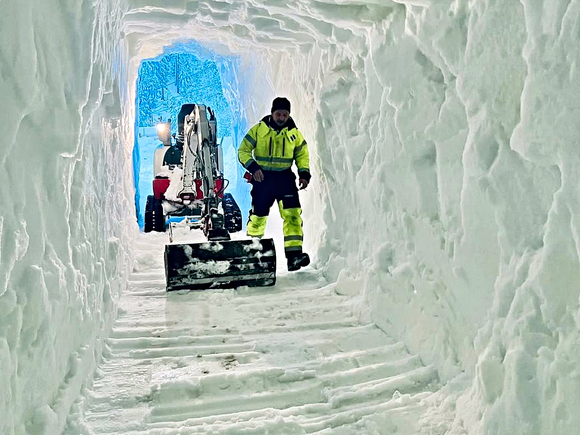 Pohlad z vnutra vyhlbenej kopy snehu, minibager a clovek v jaskyni